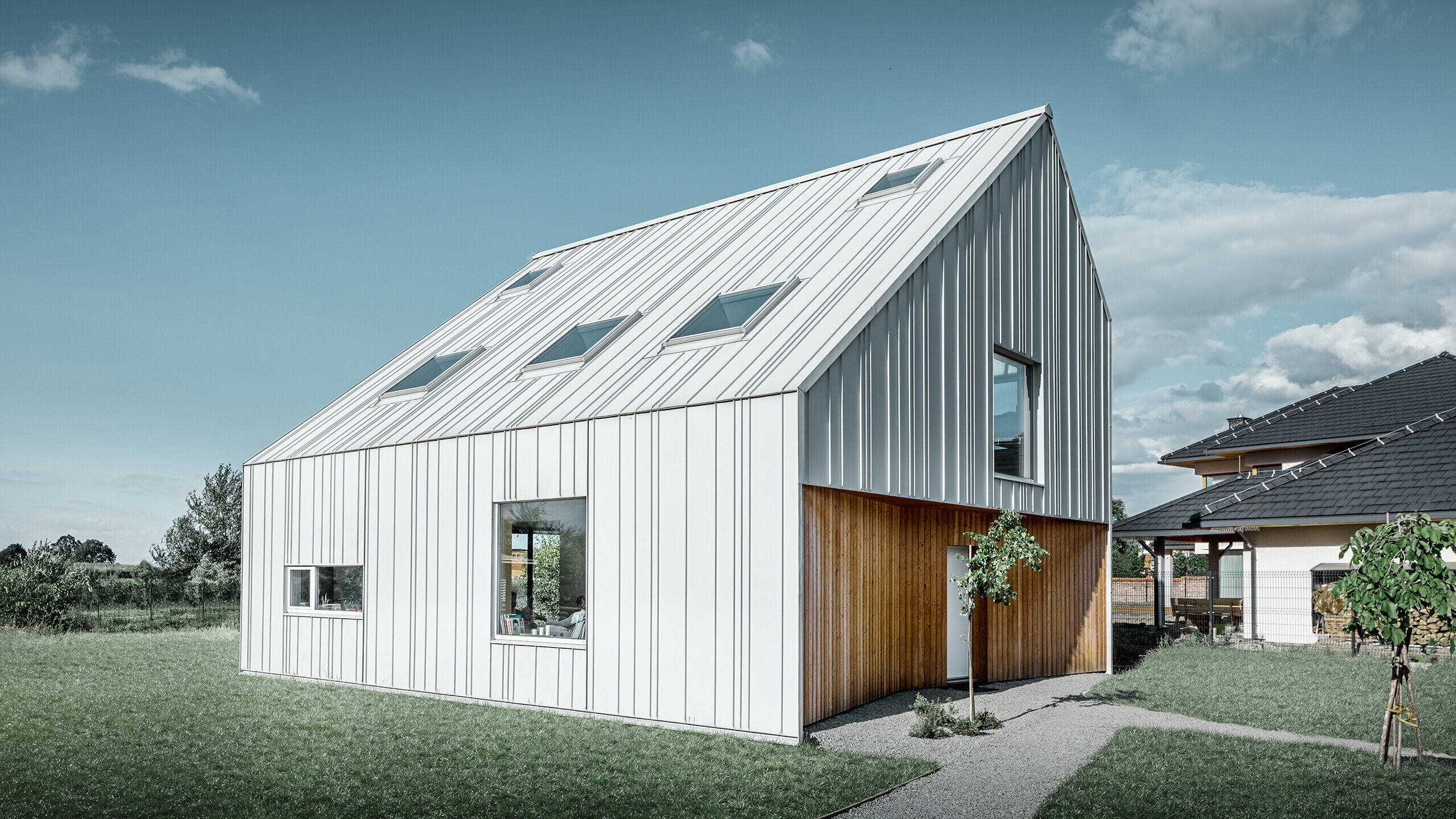 Modern detached house with gable roof, the entire outer skin is clad with PREFALZ standing seam in PREFA white. The panels of different widths extend from the roof over the façade. Several roof windows are installed in the roof.