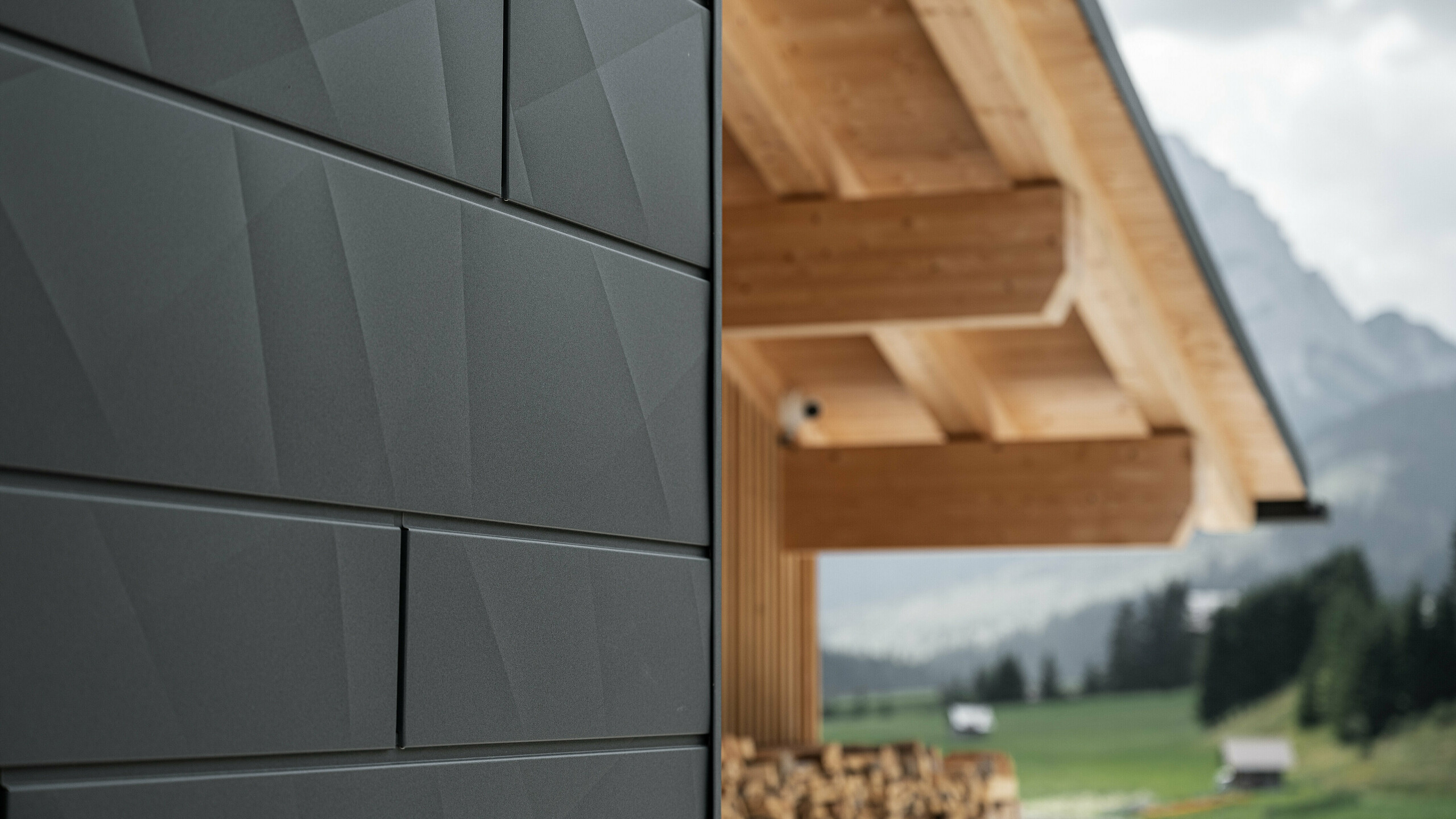 Close-up of the Siding.X façade panels in P.10 black from PREFA on Casa Hoffe in Sappada, Italy. The aluminium façade system has been skilfully installed in a modern, abstract design that forms an attractive contrast to the visible wooden elements of the roof structure. The innovative façade solution blends seamlessly into the alpine ambience and represents the combination of functionality, durability and aesthetic building culture.