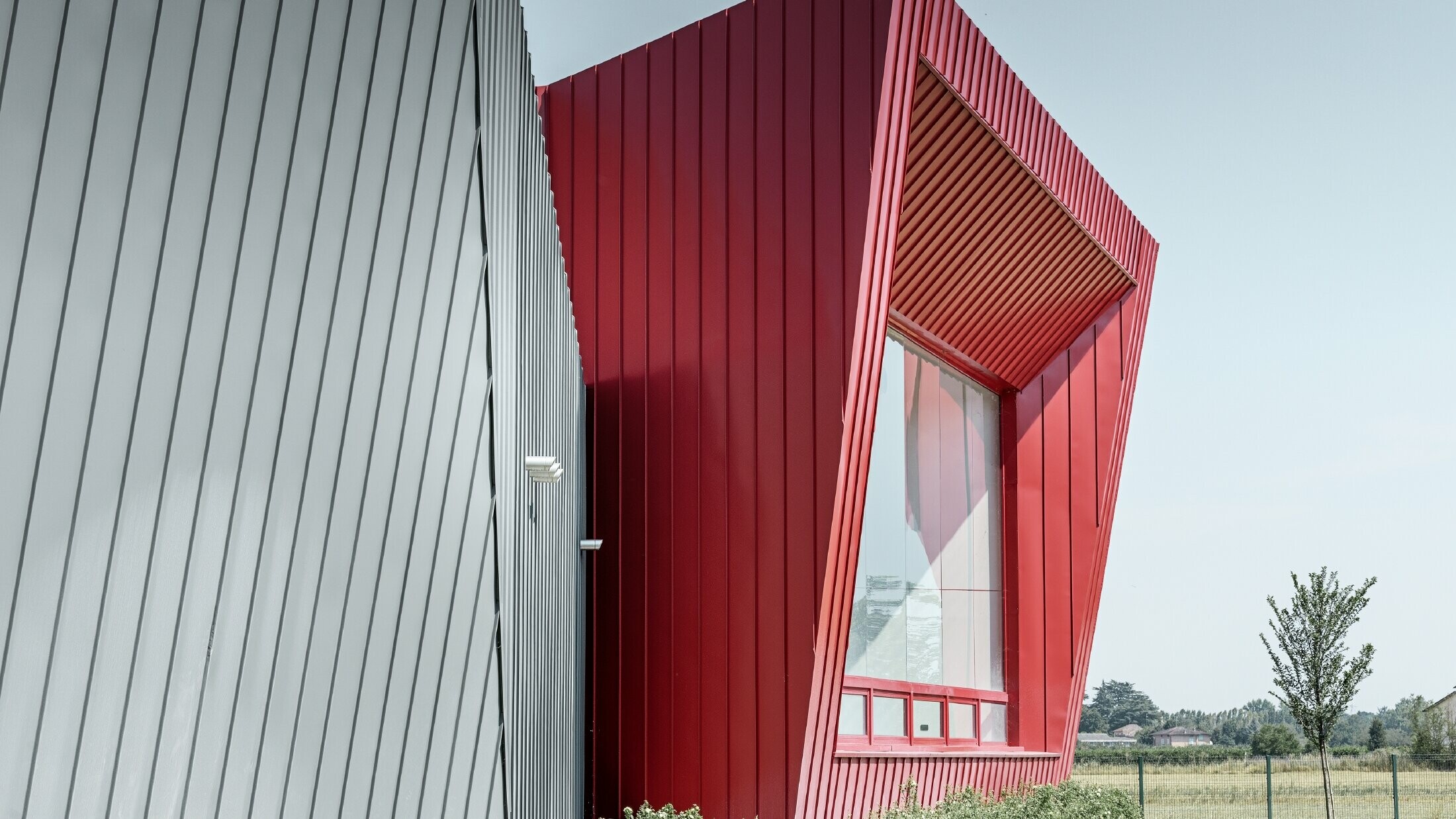 modern training centre by Dieci in Montecchio Emilia, Italy, with grandstand with aluminium façade with Prefalz standing seam in light grey and Falzonal in carmine red 