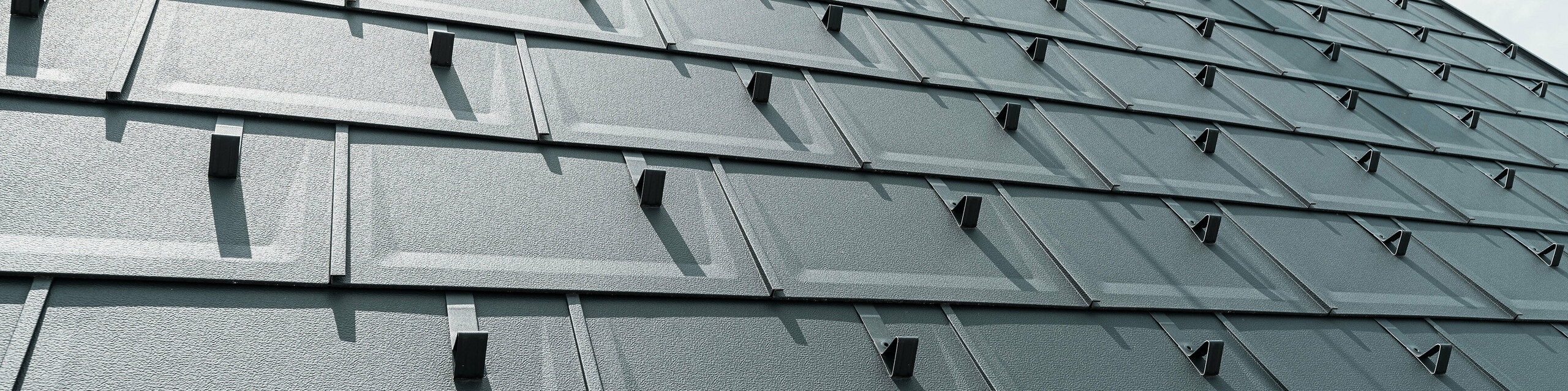 Detailed view of the PREFA R.16 roof tile in colour P.10 anthracite. PREFA snow guards and a smoke hood can be seen on the roof.