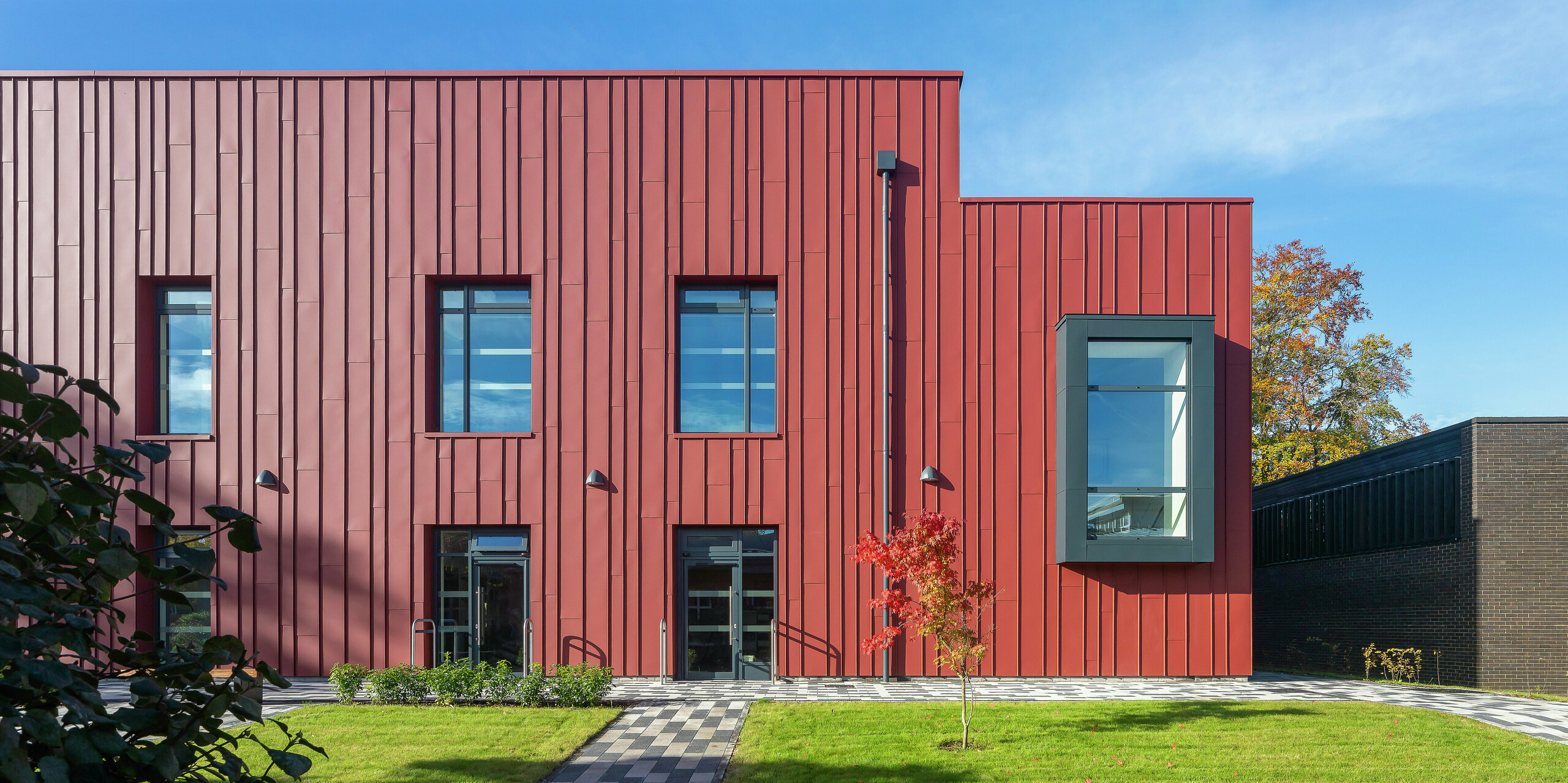 Modern architecture with PREFALZ: The façade of the Soldiers' Centre in Pirbright impresses with elegant standing seam cladding made of PREFALZ in P.10 oxide red. The stylish window framing in P.10 anthracite sets deliberate accents and gives the building a dynamic appearance. Long-lasting, aesthetic and sustainable - PREFA aluminium products for innovative building concepts.