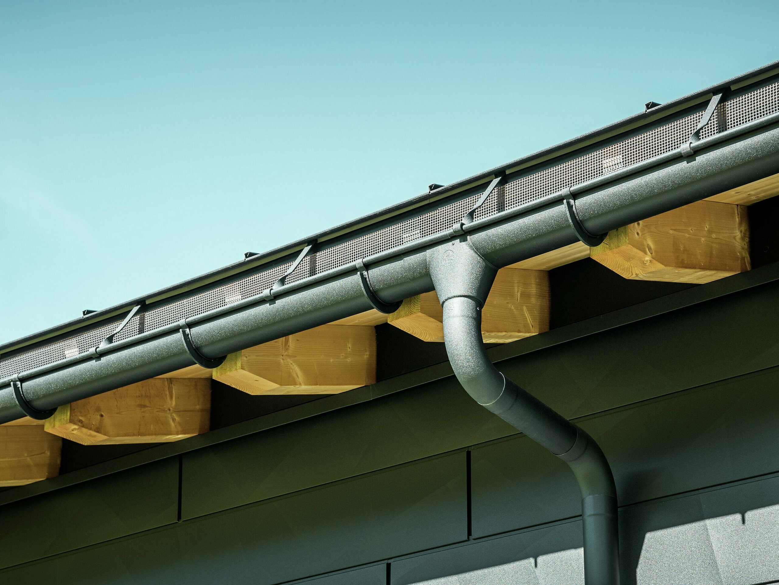 Close-up of the façade of a modern detached house in Ascharina, Switzerland. The sides of the building were clad with striking PREFA Siding.X façade panels in P.10 black. The PREFA roof drainage system with half-round gutter and downpipe is colour-coordinated.