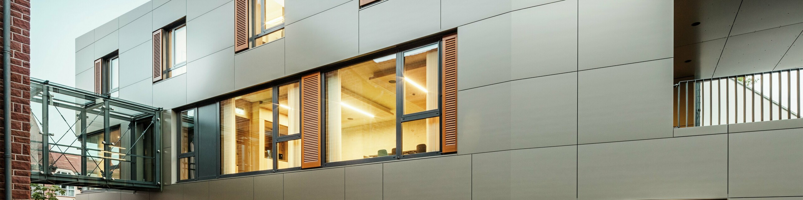 Modern façade on the town hall in Alzenau, Germany, featuring PREFA aluminium composite panels in bronze, combined with window shutters and green planting areas. The high-quality aluminium cladding ensures an elegant, durable appearance and is ideal for sustainability construction projects. The side is clearly visible here.