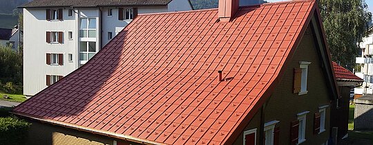 Gable roof covered with PREFA aluminium roof tiles. Brick-red roof with snow guards and chimney
