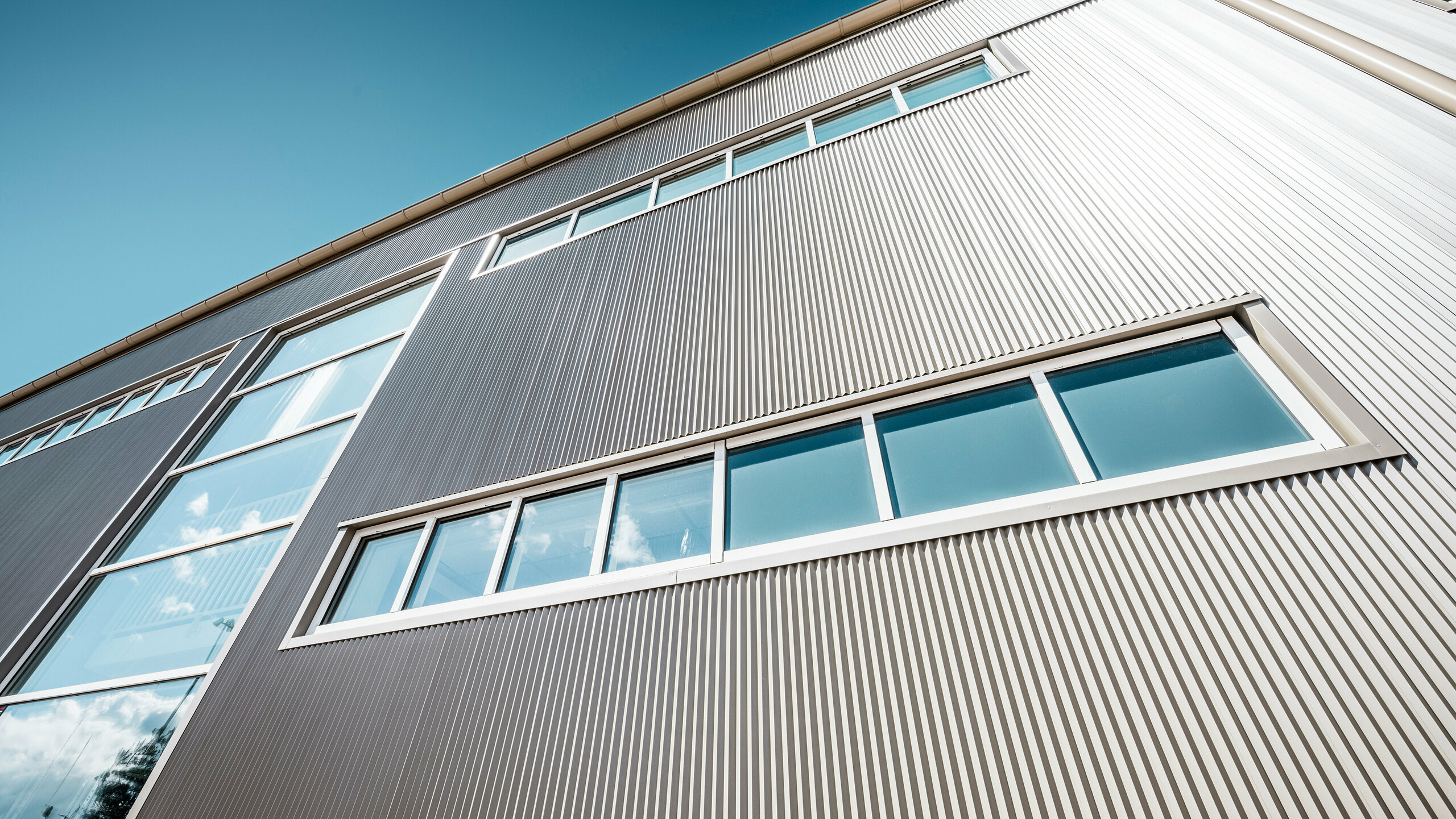 Exterior view of the Park Arena in Värnamo, Sweden, with a modern PREFA façade in bronze. The serrated aluminium profiles create striking light and shadow effects. The recessed windows blend harmoniously into the precisely crafted façade, which stands for durability, resilience and contemporary design.
