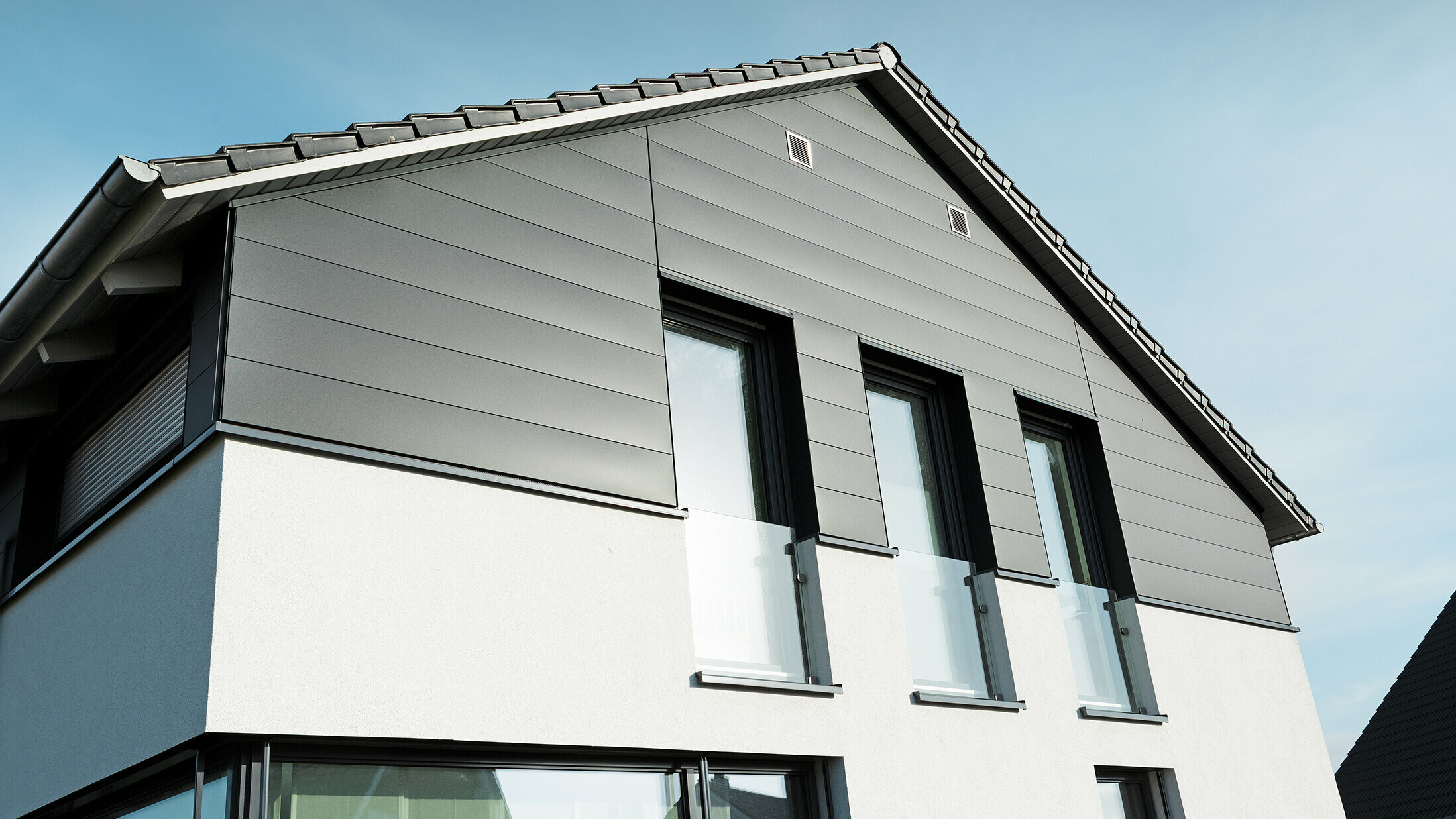 Moderne Hausfassade in Isenbüttel mit PREFA Sidings in P.10 Anthrazit – die Aluminiumverkleidung verleiht dem Einfamilienhaus einen eleganten und wetterfesten Look. Die vertikalen Fenster betonen die moderne Architektur zusätzlich.