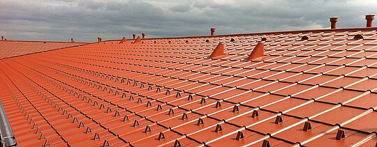 Close-up of a PREFA tile-effect aluminium roof - PREFA roof tiles in brick red with snow guards