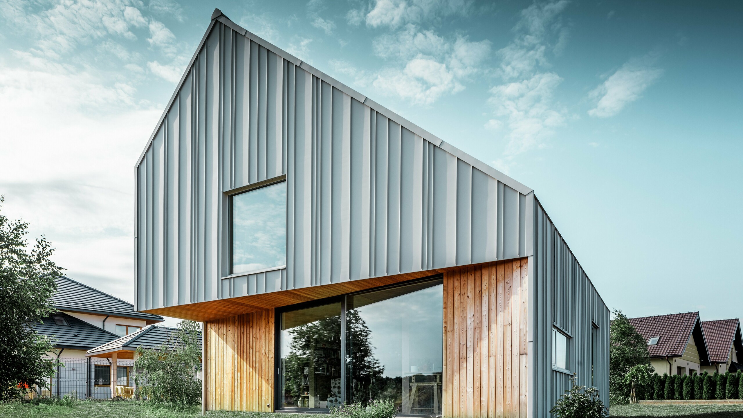 Modern detached house with gable roof without eaves and aluminium façade by PREFA in white. In addition, a wooden façade with vertical wooden panels is combined on the ground floor. 