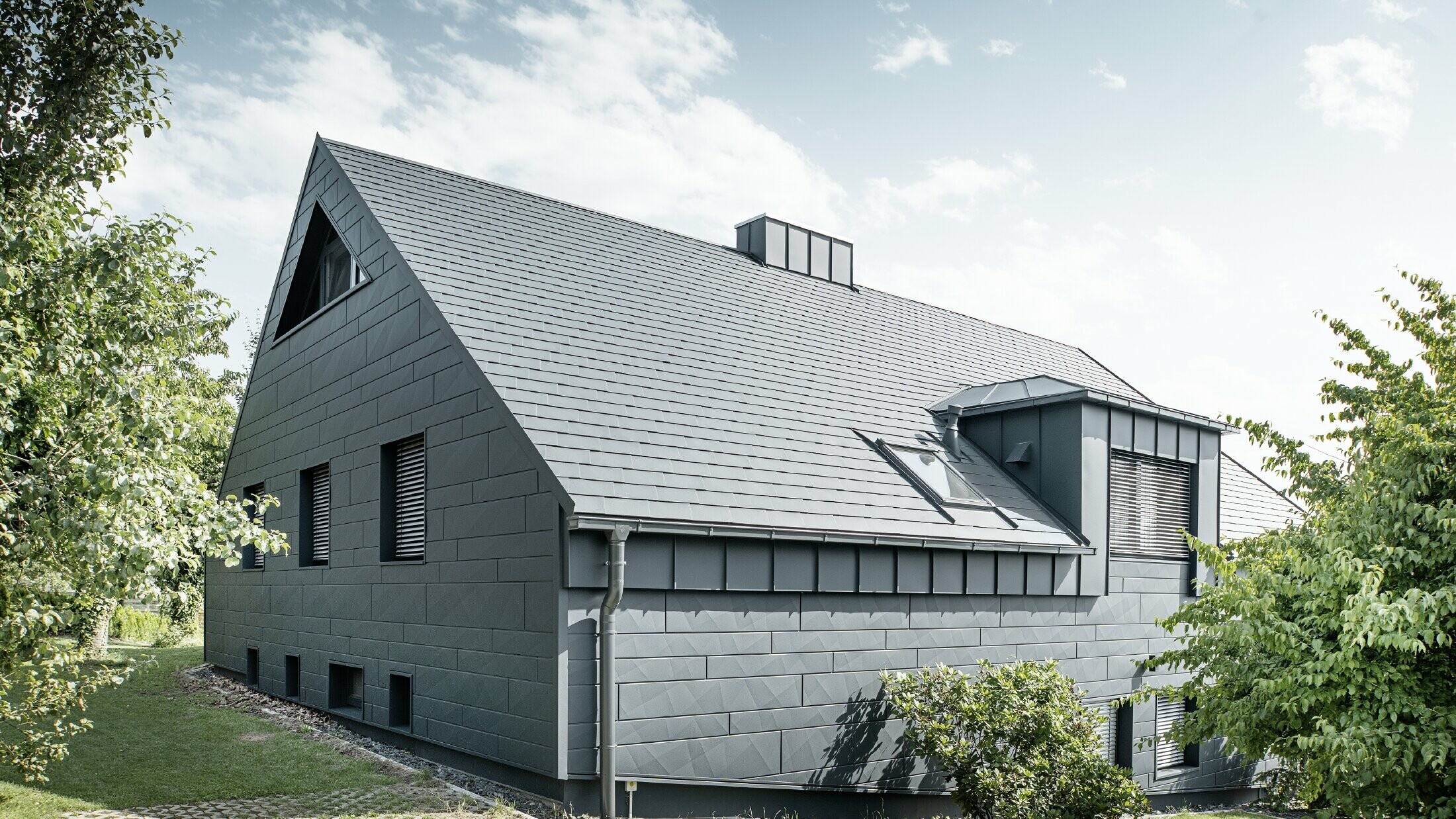 Large detached house with a gabled roof and lots of windows. The entire house was clad with an anthracite aluminium shell, PREFA aluminium shingles were used on the roof and Siding.X in anthracite on the façade.