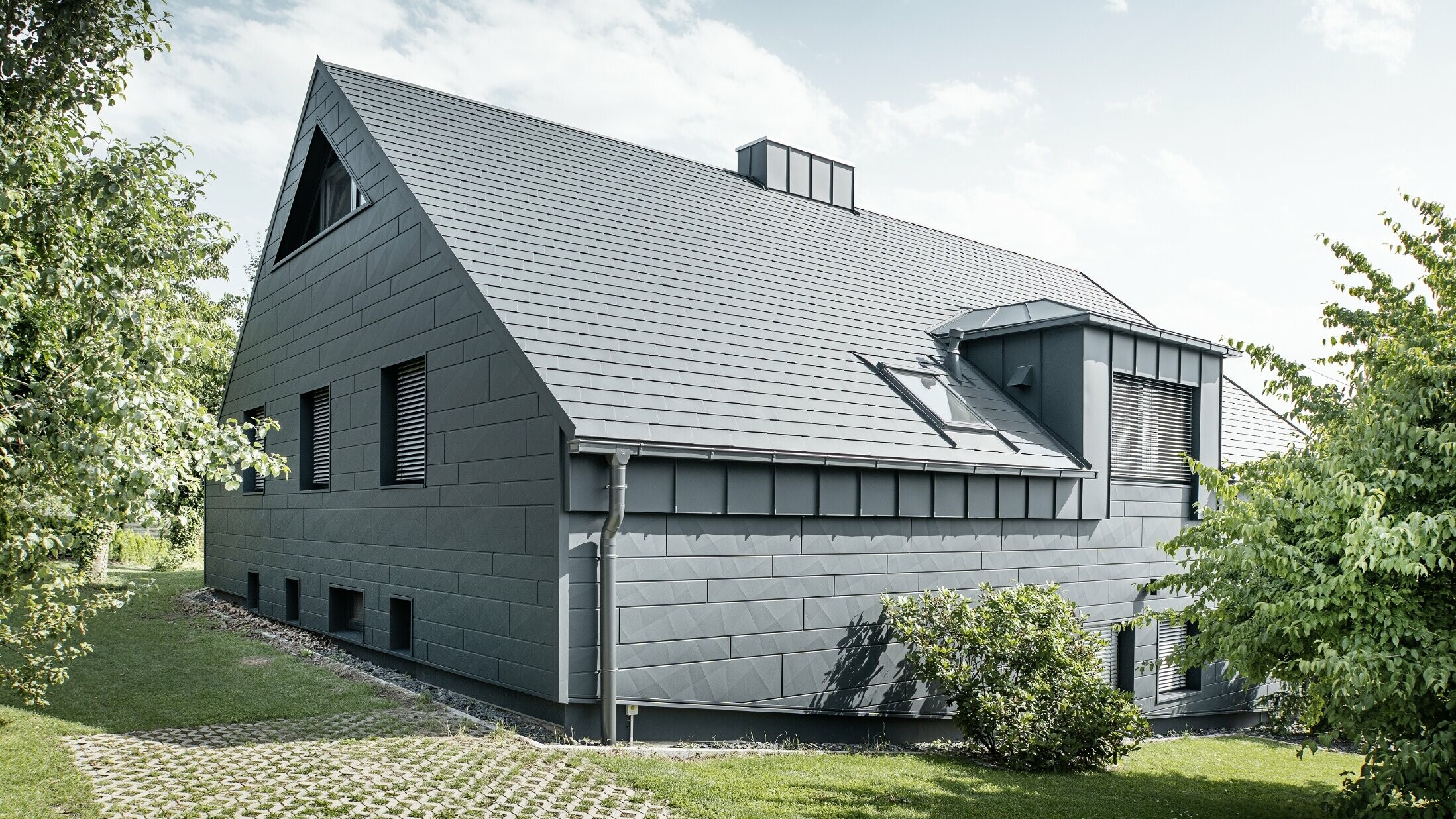Large detached house with a gabled roof and lots of windows. The entire house was clad with an anthracite aluminium shell, PREFA aluminium shingles were used on the roof and Siding.X in anthracite on the façade.