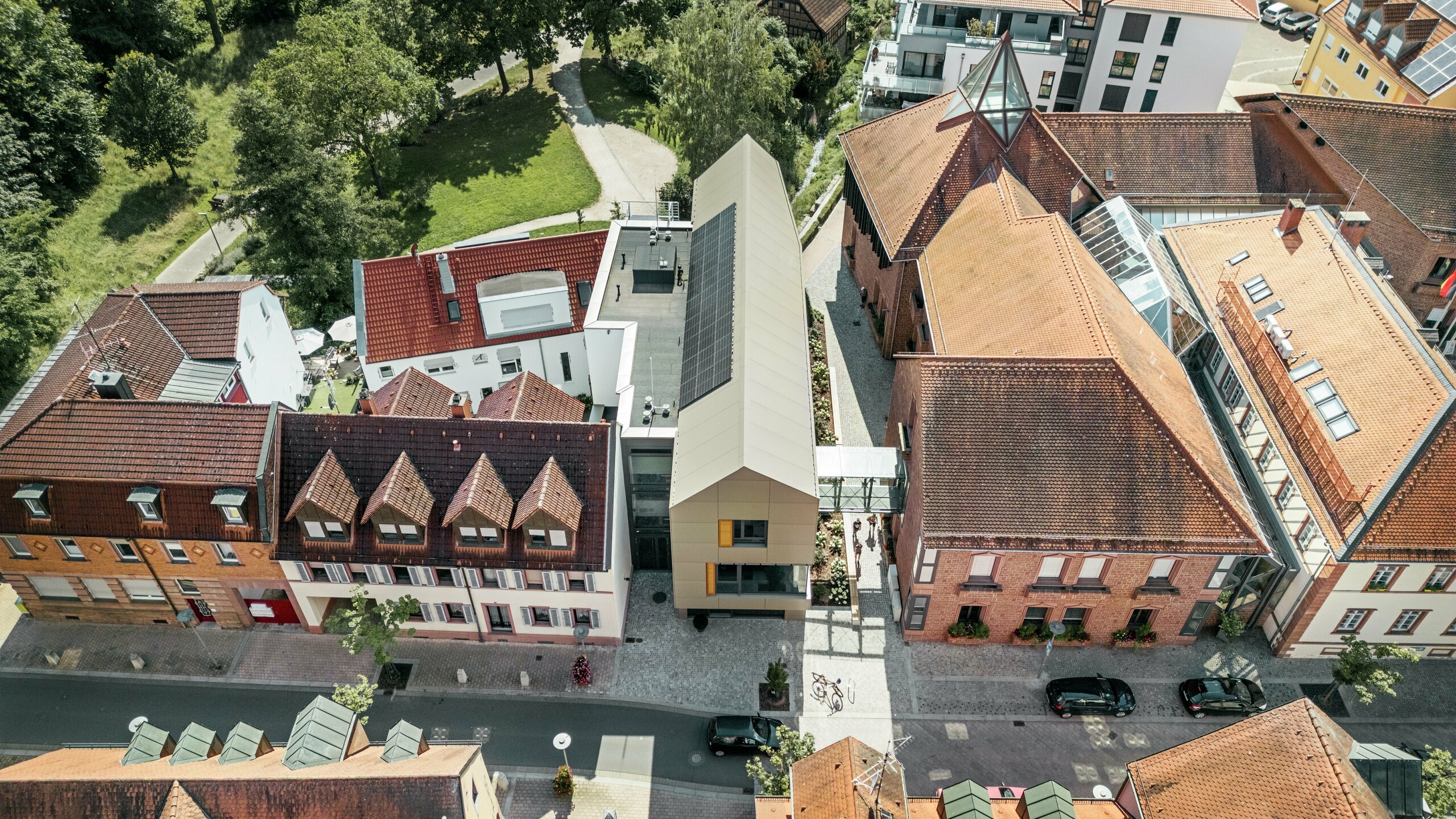 The town hall in Alzenau, Germany, is located in the centre of a historic townscape, surrounded by traditional buildings with red tiled roofs. In contrast, the modern town hall has a façade clad in PREFA aluminium composite panels in an elegant bronze tone. The innovative architecture clearly stands out from the neighbouring classic buildings, yet blends harmoniously into the townscape.