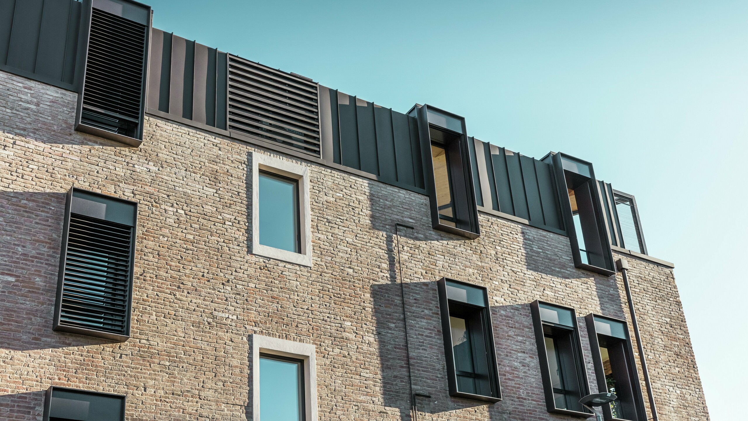 Detailansicht eines renovierten Backsteinhauses in Italien mit PREFALZ Aluminiumdach in P.10 Nussbraun und modernen Fenstergauben – gelungene Kombination aus traditioneller Ziegelbauweise und zeitgemäßer Architektur