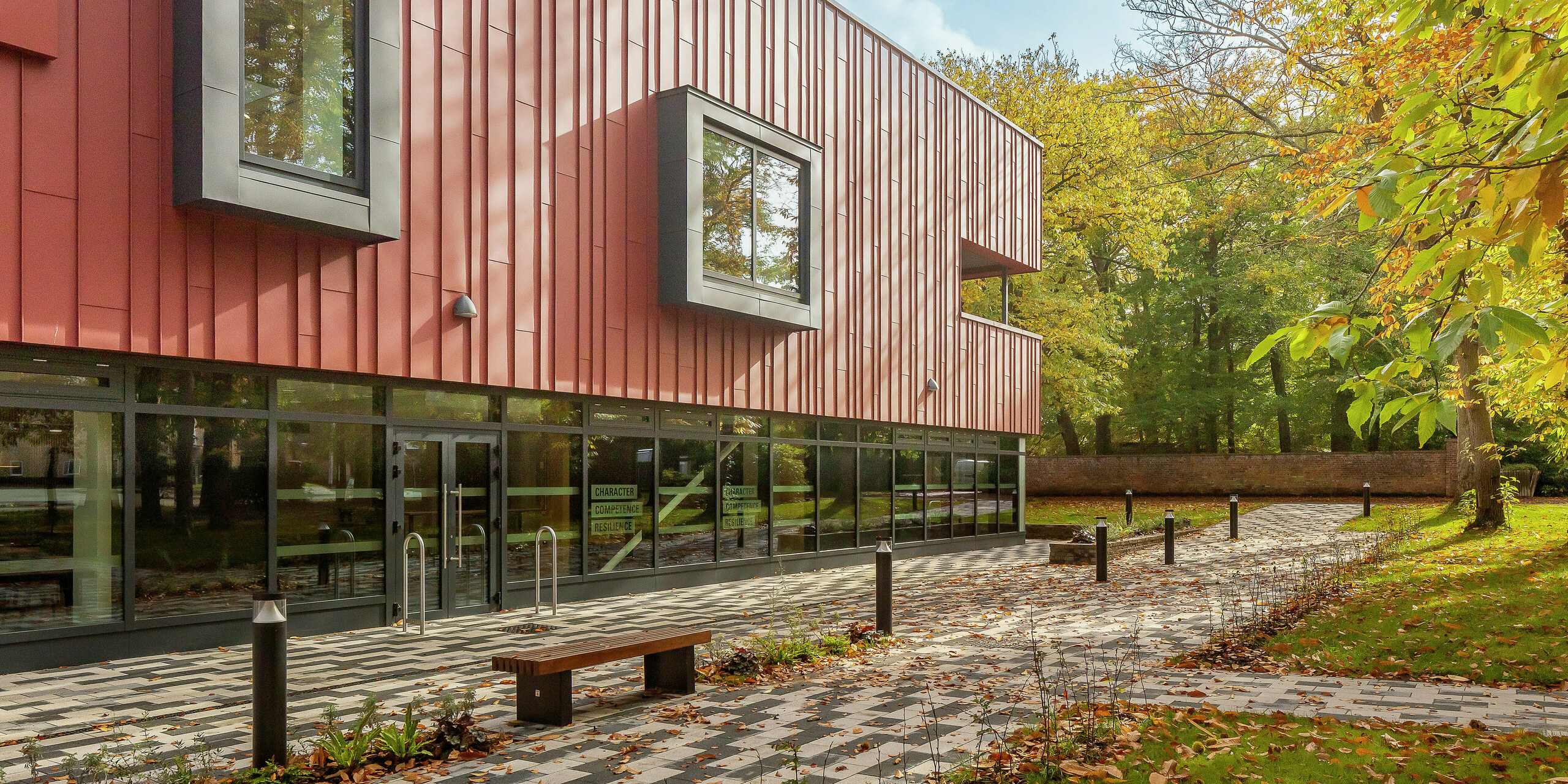 Harmonious architecture in a green setting: the modern standing seam façade of the Soldiers' Centre in Pirbright is made of PREFALZ in P.10 oxide red. The robust aluminium cladding blends perfectly into the autumnal surroundings. Striking, cantilevered window frames in P.10 anthracite set stylish accents. Large glass surfaces on the ground floor ensure transparency and openness. The paved forecourt with a bench invites you to linger – a successful combination of design, functionality and nature.