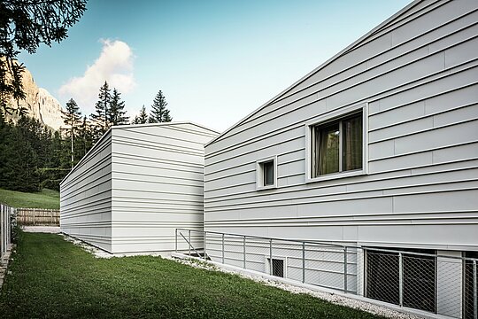 The rear of the Tempesti barracks in Corvara offers a striking view: forest trees, a bright blue sky and mountains highlighted by the sun. The light aluminium façade with its clear structure showcases the technical sophistication of PREFALZ in the colour P.10 PREFA white. The horizontal aluminium panels reflect the light, offer optimum weather protection and blend harmoniously into the Alpine environment. A prime example of durable and modern military architecture!