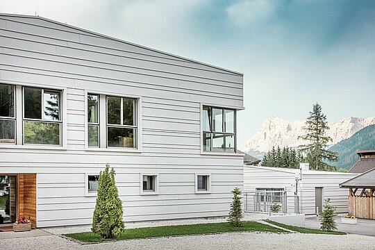 Detailed view of the Tempesti barracks with precisely laid PREFALZ sheets in colour P.10 PREFA white. The clear lines of the horizontally laid standing seam roofing emphasise the modern façade design. The light-coloured surface reflects sunlight and optimises the microclimate. The impressive South Tyrolean mountains rise up in the background – this is where technology meets nature at the highest level.