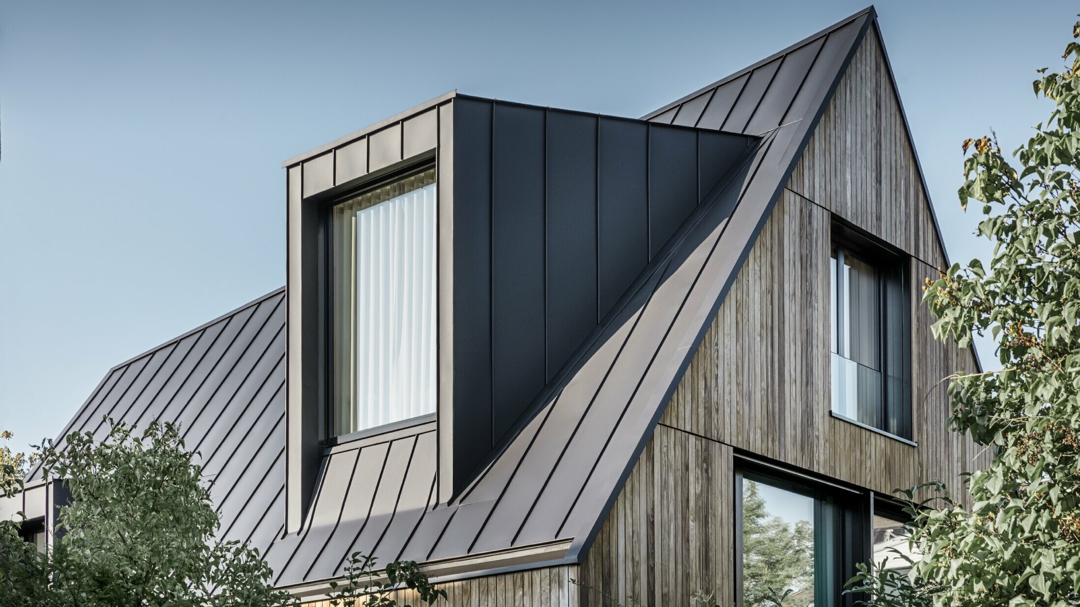 Steep gable roof with large dormer, covered with PREFALZ by PREFA in anthracite standing seam roof combined with wooden façade
