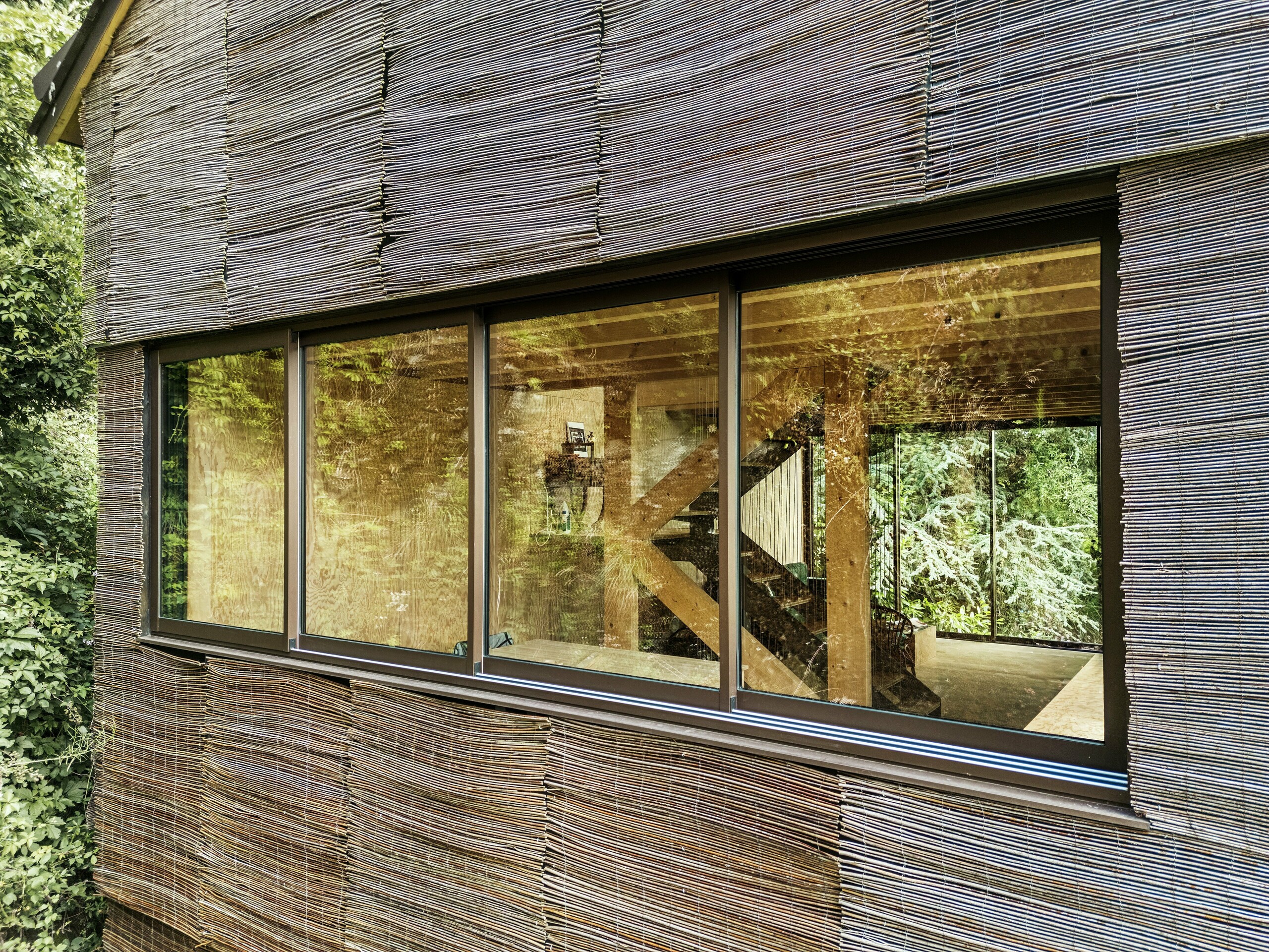 Detail eines modernen Aluminiumrahmenfensters mit Weidenholzfassade an einem Haus in Frankreich – nachhaltiges Design mit PREFA-Dachschindeln und natürlicher Umgebung.