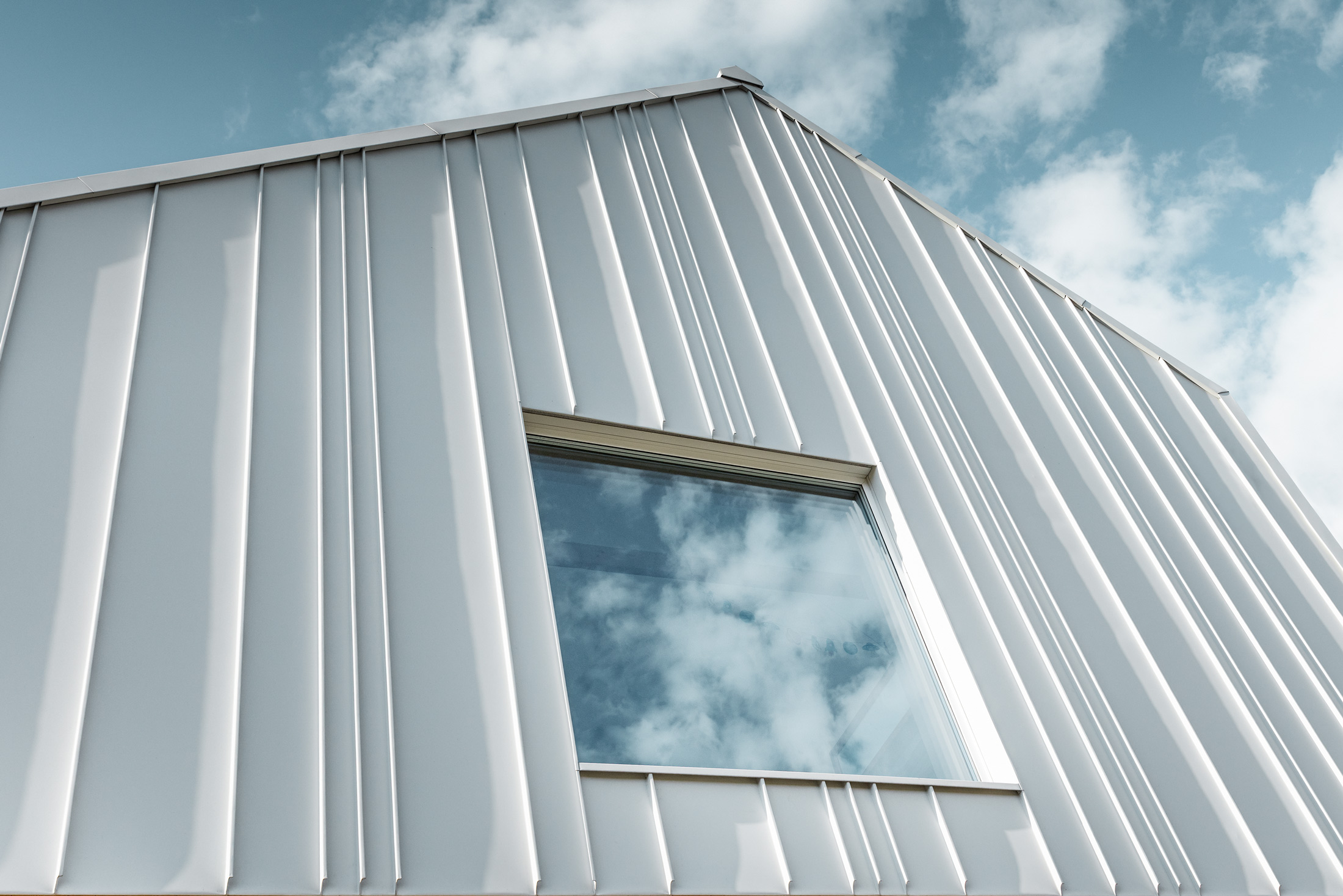 white PREFALZ as angled standing seam on the façade with different panel widths and a window